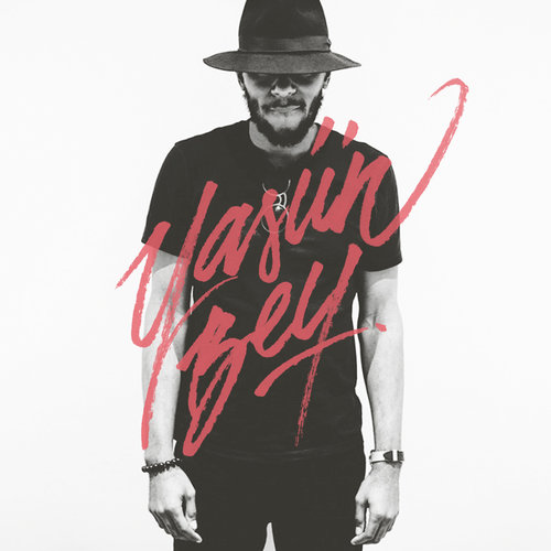 Portrait of a man with a beard wearing a hat and a black t-shirt, with red cursive overlay text against a white background.