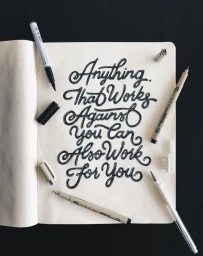 Hand-lettered quote Anything That Works Against You Can Also Work For You in a notebook with pens