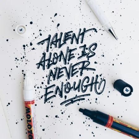 Hand-lettered quote Talent alone is never enough in black ink surrounded by ink splatters and pens on paper.