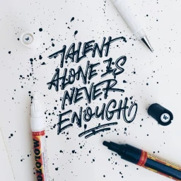Hand-lettered quote Talent alone is never enough in black ink surrounded by ink splatters and pens on paper.