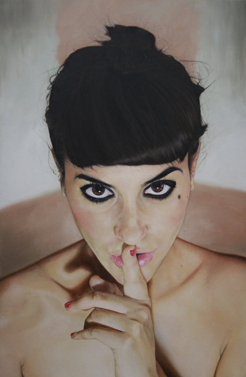 Portrait of a brunette woman with dark eyeliner holding a finger to her lips in a shushing gesture, against a neutral backdrop.