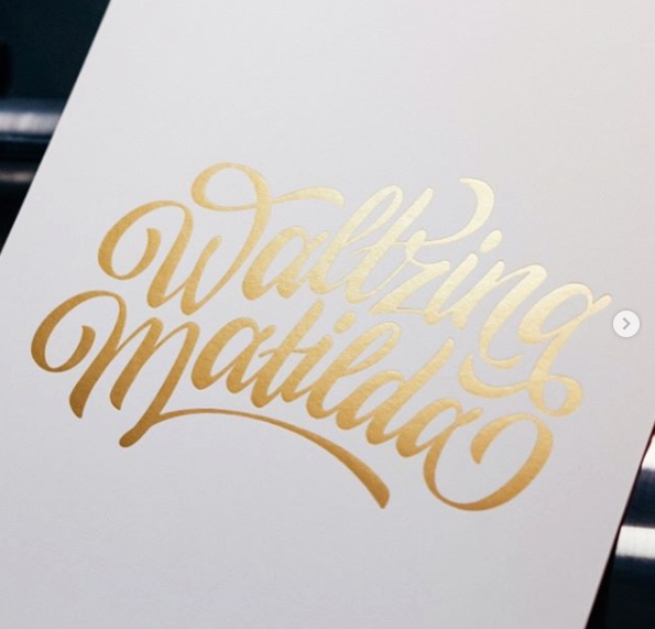 Elegant calligraphy art featuring the name 'Waltzing Matilda' in a flowing, golden script against a clean white background.