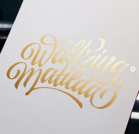 Gold foil lettering reading Waltzing Matilda on a cream paper surface by illustrator Dave Coleman.
