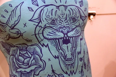 Close-up of a teal torso sculpture featuring intricate purple ink line drawings of a roaring tiger head, a bird, and a blooming rose.