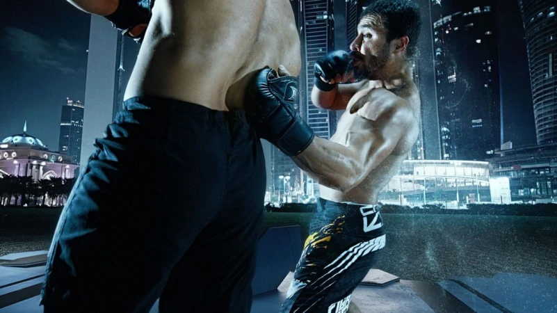 Two shirtless male athletes are engaged in a combat sports match in an urban setting at night, with skyscrapers in the background.