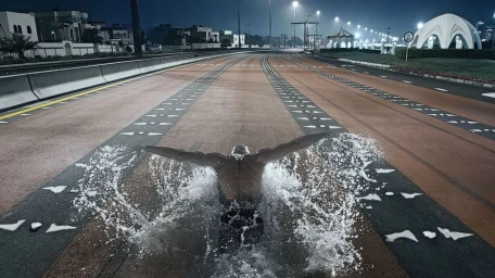Swimmer doing butterfly stroke on an asphalt road at night with streetlights illuminating the scene