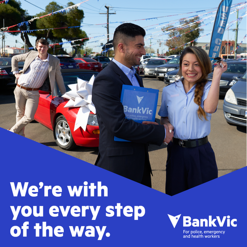 Car dealership scene with two adults shaking hands; another man stands by a red car with a large bow on its hood; BankVic logo.