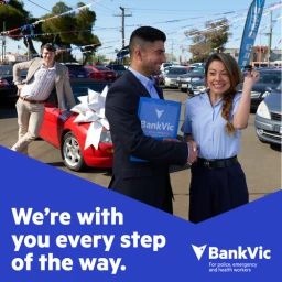 BankVic car purchase commercial scene with a smiling customer holding keys and a representative shaking hands in Sydney.