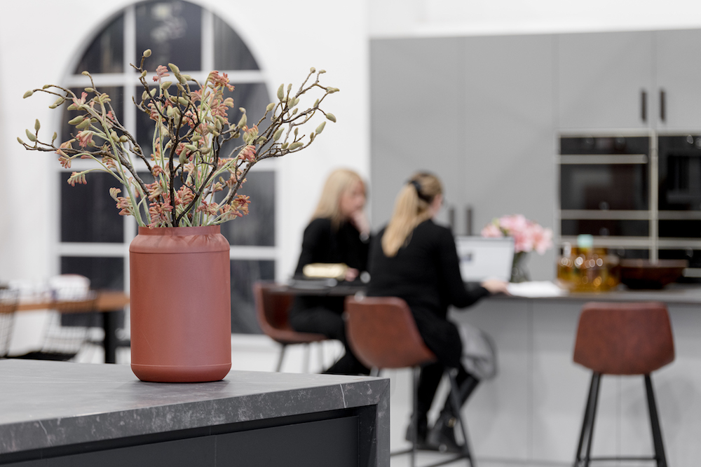 Interior view of a modern kitchen with a vase of flowers on a countertop and two women in the background at a kitchen island.