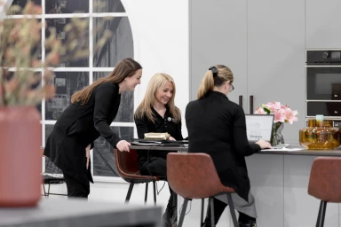 Three women working in a modern kitchen interior with grey cabinetry and a large arched window in Melbourne by Glue Content.