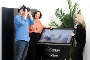 Man wearing VR headset next to woman leaning on touch screen kiosk and another woman standing beside it