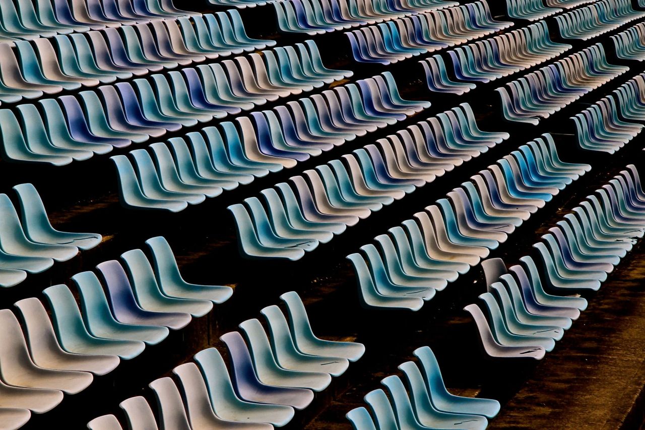 Rows of light blue stadium seating in an angled overhead shot. The repetitive pattern creates a sense of vastness and order.