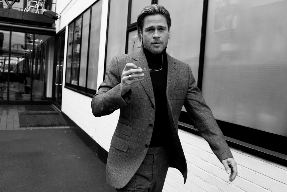 Black and white portrait of a mature adult male wearing a suit, holding glasses, and walking in an urban environment.