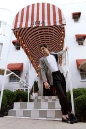 Man wearing a houndstooth blazer and white t-shirt leaning against a striped awning post