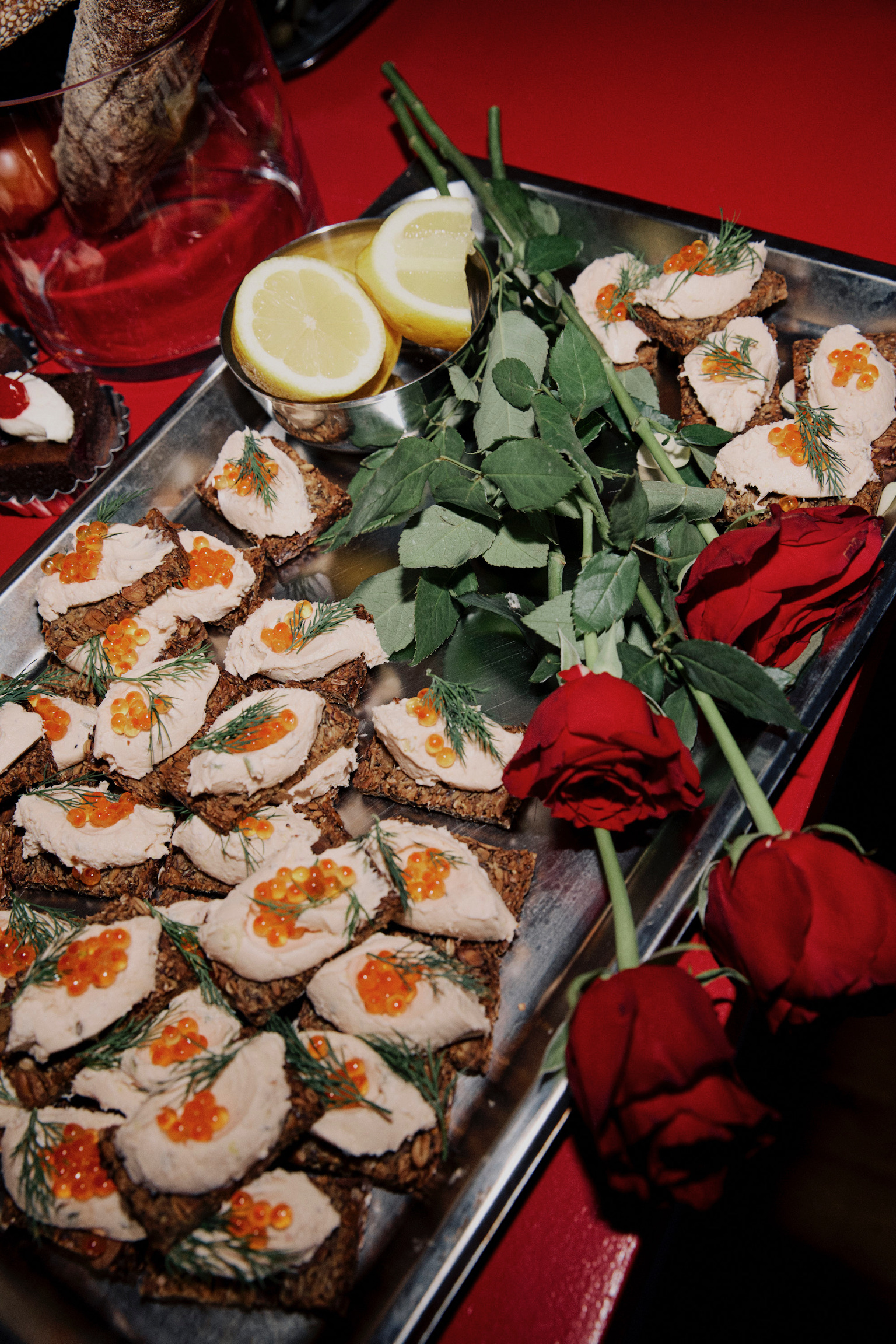 Appetizers with caviar and cream cheese served on a silver tray, garnished with dill and accompanied by lemon slices and red roses.
