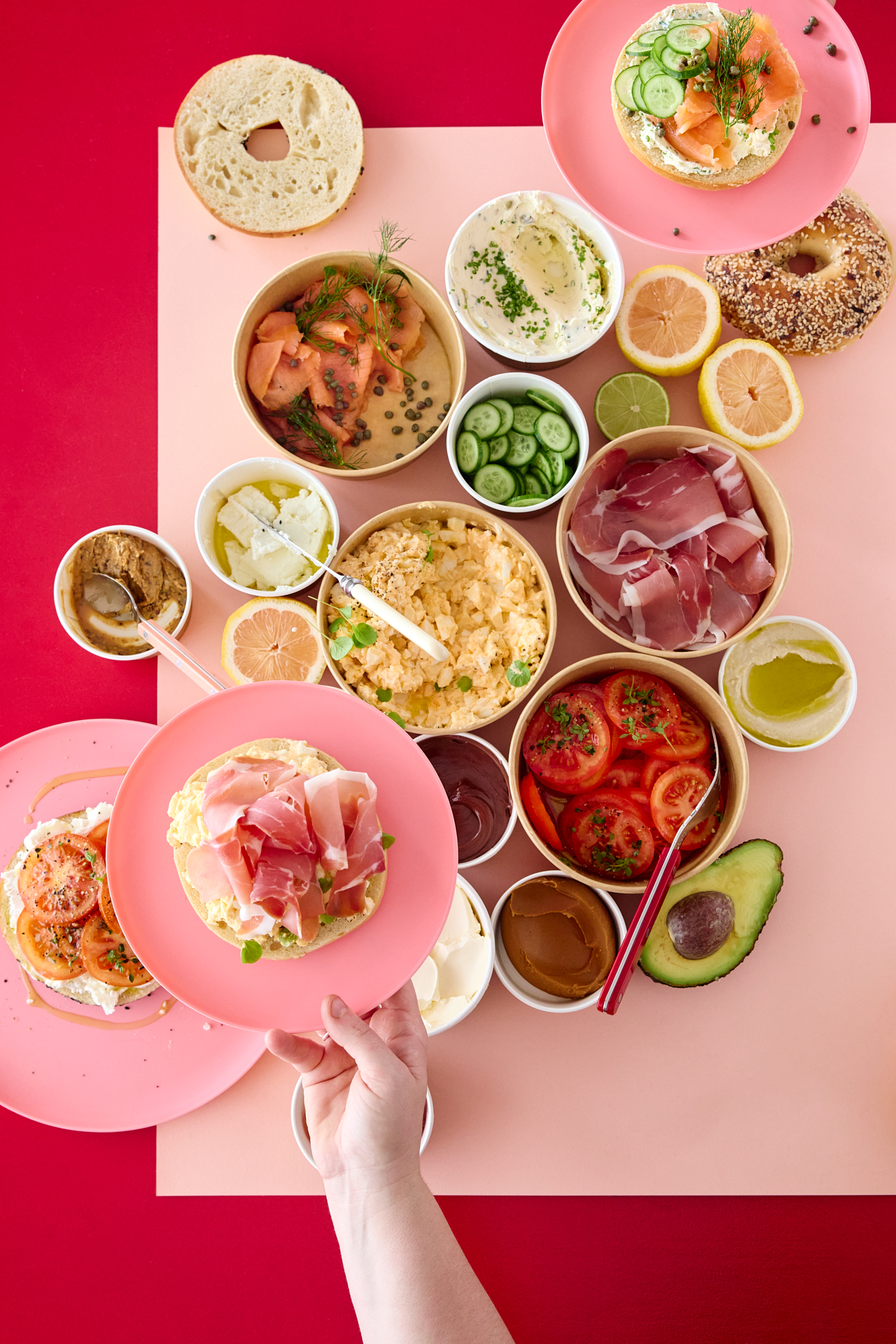 Overhead shot of bagels and various toppings displayed on a pink and red background, showcasing a variety of food options.