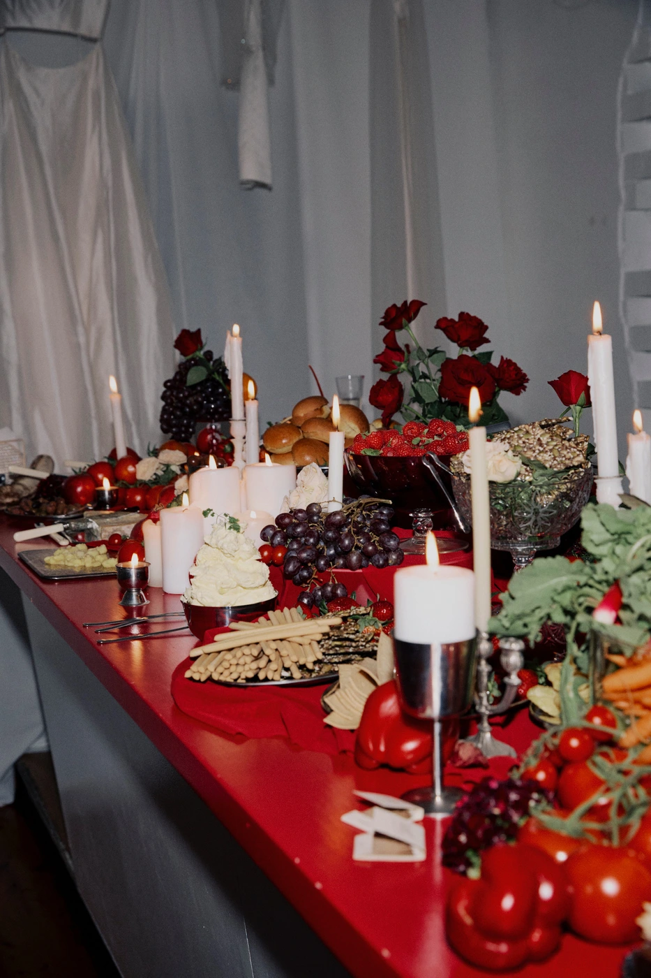 Elaborate banquet table spread in Sydney featuring lit candles, red roses, grapes, and breadsticks on a red surface.