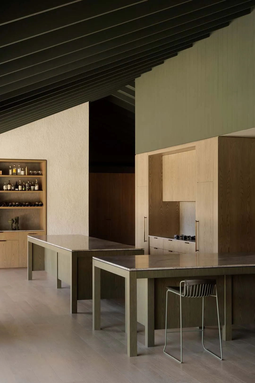 Modern kitchen interior featuring minimalist islands, light wood cabinets, bar stool seating, and sleek design in a spacious setting.