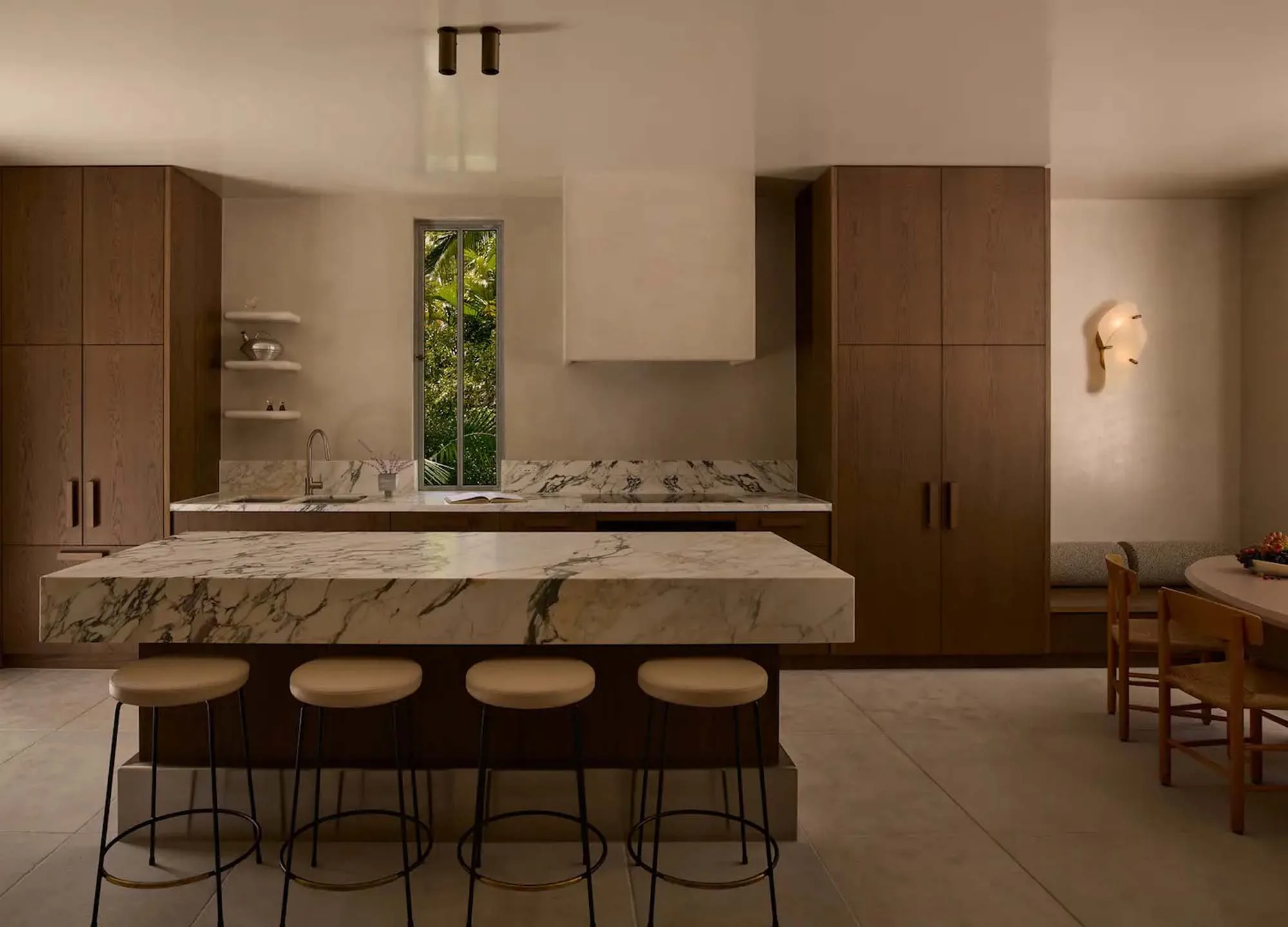 Modern kitchen interior featuring marble countertops, wood cabinetry, island with stools, and natural light from a window with green foliage.