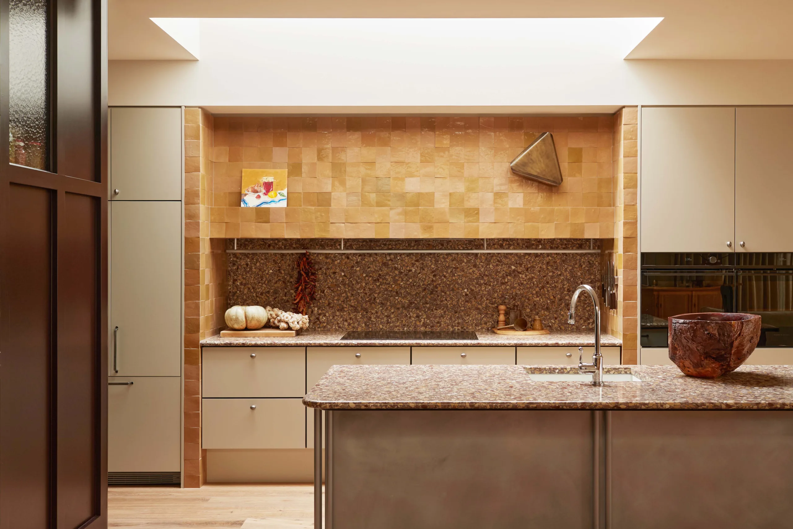 Modern kitchen interior featuring an island, tan tiled walls, stainless steel appliances, and natural light from a skylight.
