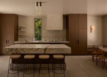 Modern kitchen featuring a thick marble island with four round barstools in front of dark wood floor-to-ceiling cabinets.