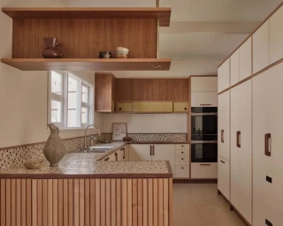 Mid-century style kitchen interior with wooden slatted counter, mosaic tile countertops, cream cabinets, and open timber shelving.