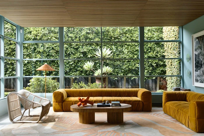 Modern living room with mustard yellow tufted velvet sofas, an oval wooden coffee table, and large windows overlooking a garden.