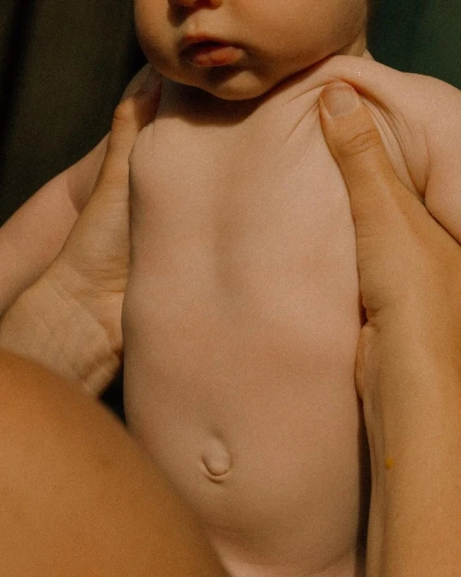Infant in arms with focus on the baby's torso and parent's hands, captured in a close-up shot with natural light.