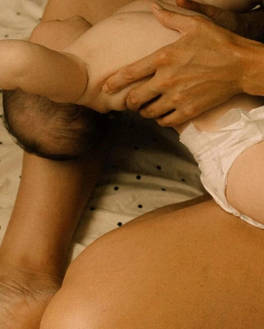 Close-up of a baby lying on an adult's lap, showcasing the baby's diaper and the adult's arm and torso, set against a polka dot fabric.