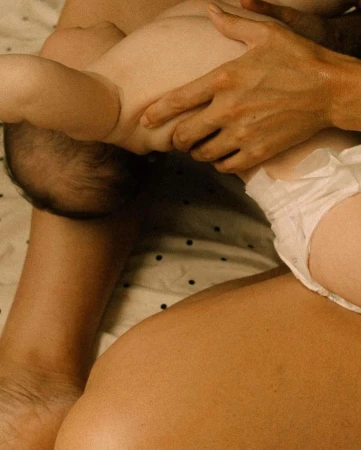 Close-up of a baby lying on an adult's lap, showcasing the baby's diaper and the adult's arm and torso, set against a polka dot fabric.