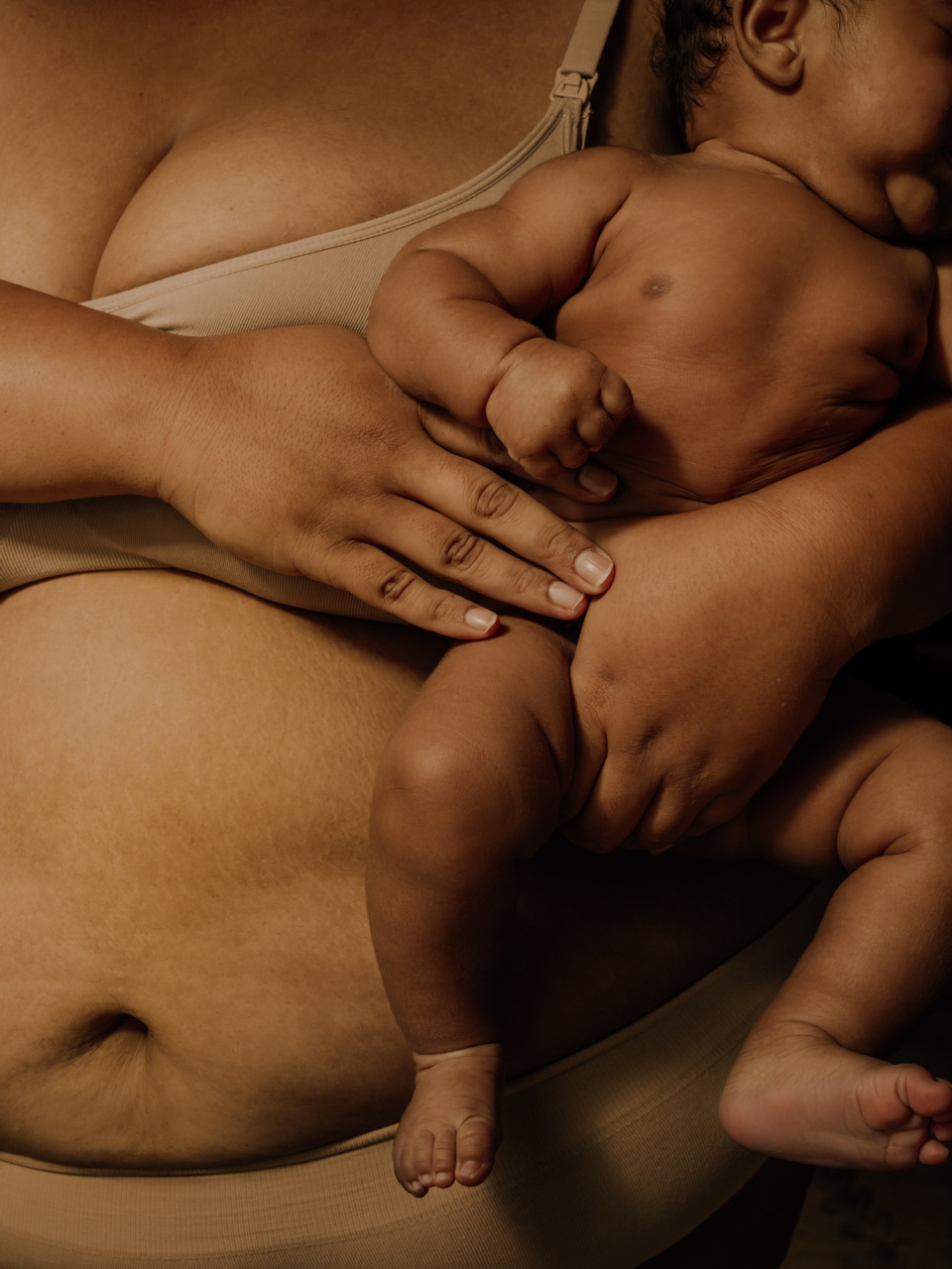 A mother holds her infant close in a warm-toned portrait focusing on the bond between parent and child, showcasing soft lighting and skin textures.
