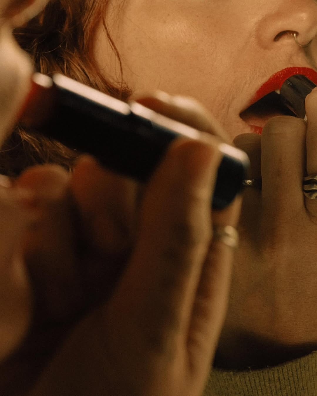 Close-up shot of fair-skinned adult female applying bright red lipstick with a dark applicator tube. The background is blurred.
