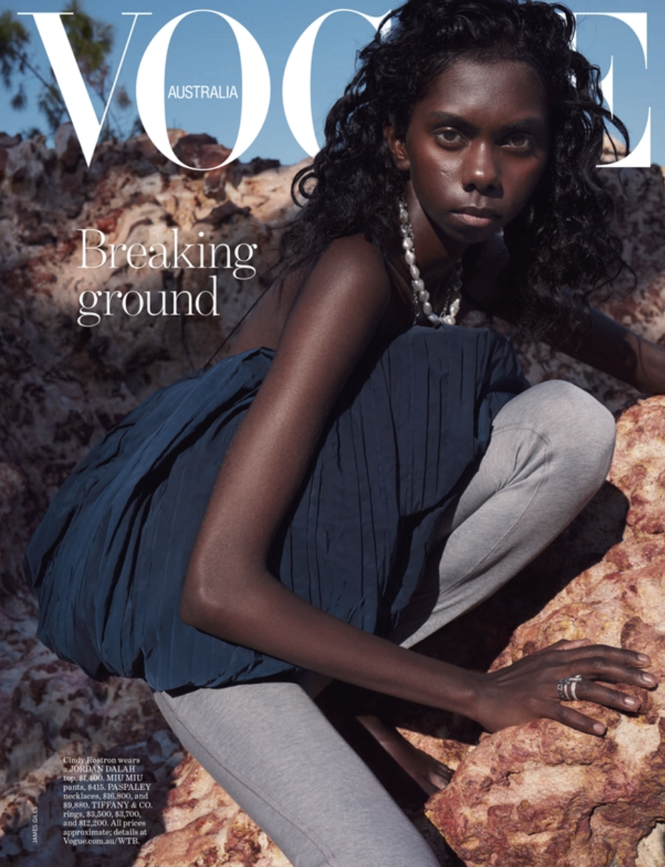 Vogue Australia magazine cover featuring an Indigenous female fashion model squatting on rocks, wearing a navy top and grey pants.
