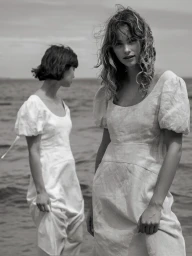 Two women in white dresses standing by the water in a black and white photograph by Peter Soulis.