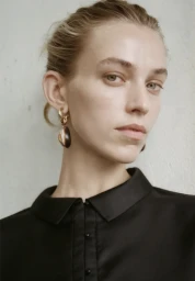 Close-up portrait of a woman wearing a black collared shirt and statement drop earrings against a neutral wall in Sydney.