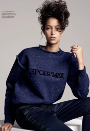 Model with voluminous curly hair wearing a dark blue sweatshirt with SPORTMAX lettering and matching trousers against a neutral background.