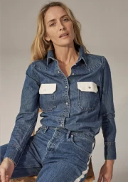 Woman in a blue denim shirt with white chest pockets and matching denim trousers against a grey backdrop