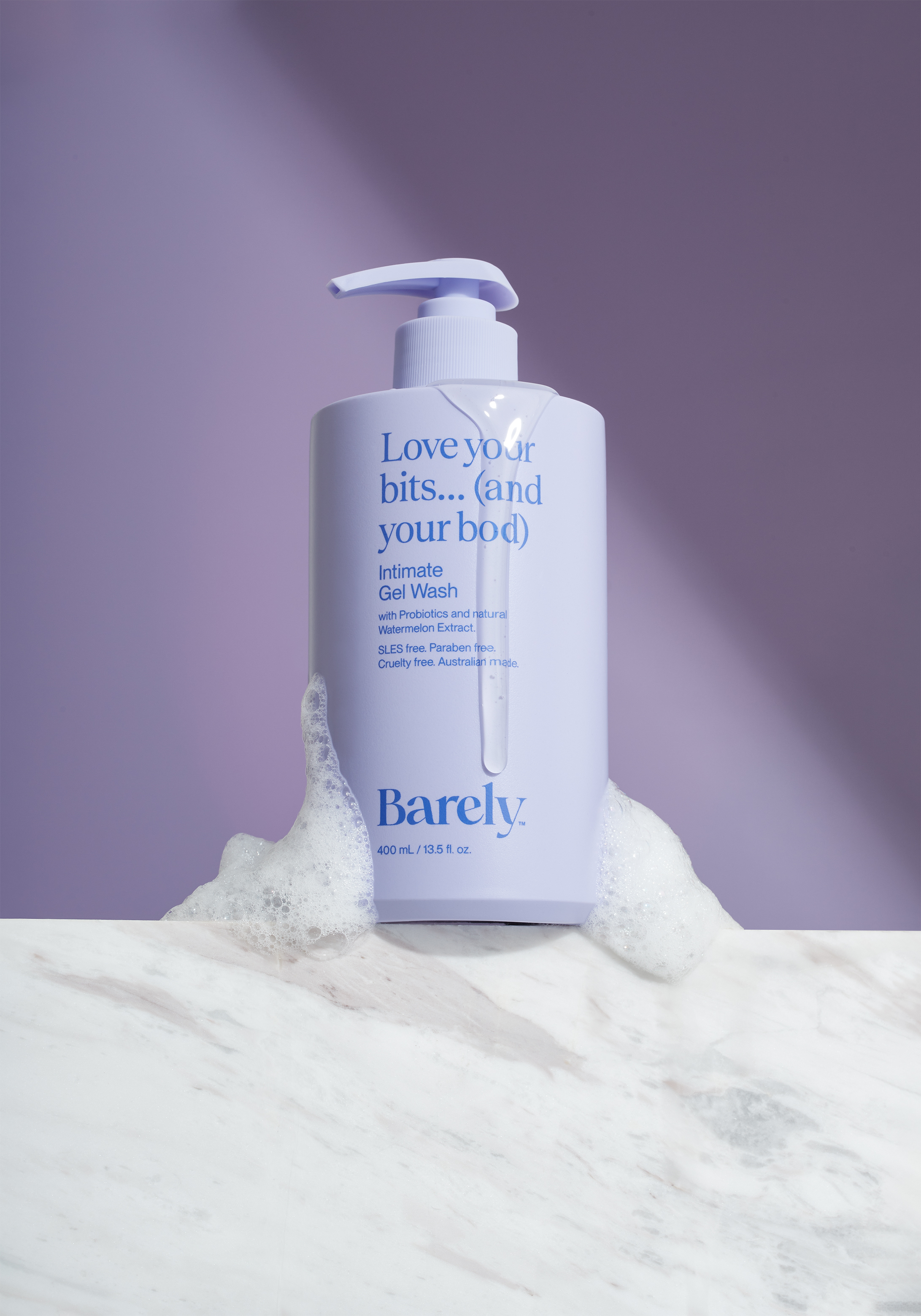 Barely brand gel wash bottle, light purple, displayed with bubbles on a white marble surface and a matching purple backdrop.