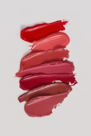 Horizontal arrangement of six smooth lipstick swatches in various shades of red, pink, and nude on a clean white background.