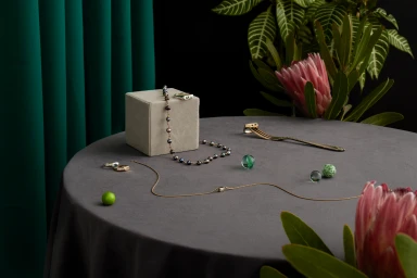Fine jewellery and pearl necklace displayed on a grey tabletop with flowers and a green velvet display box