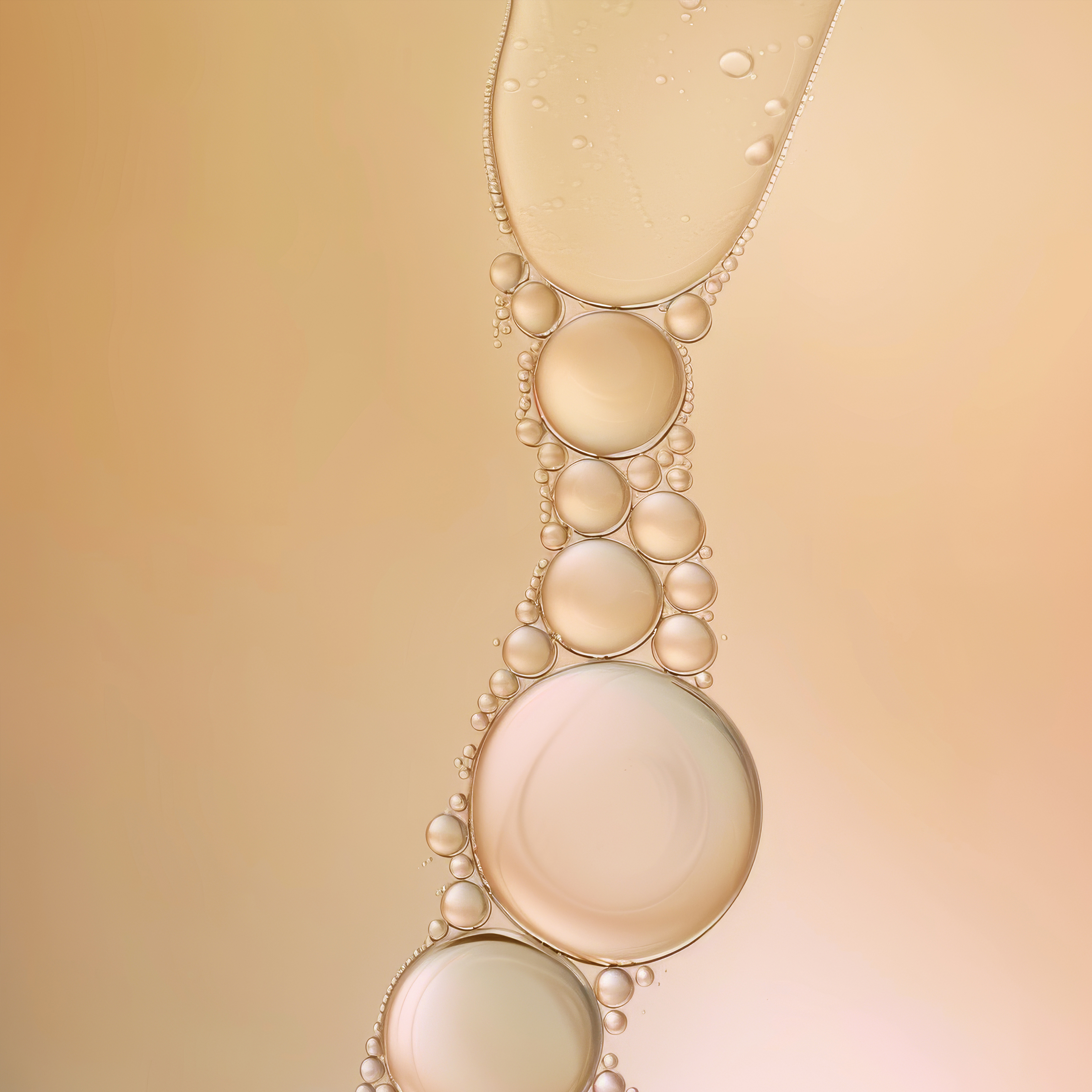 Macro image of various sized liquid bubbles in gradient of peach to cream tones forming a chain-like composition on a smooth surface.