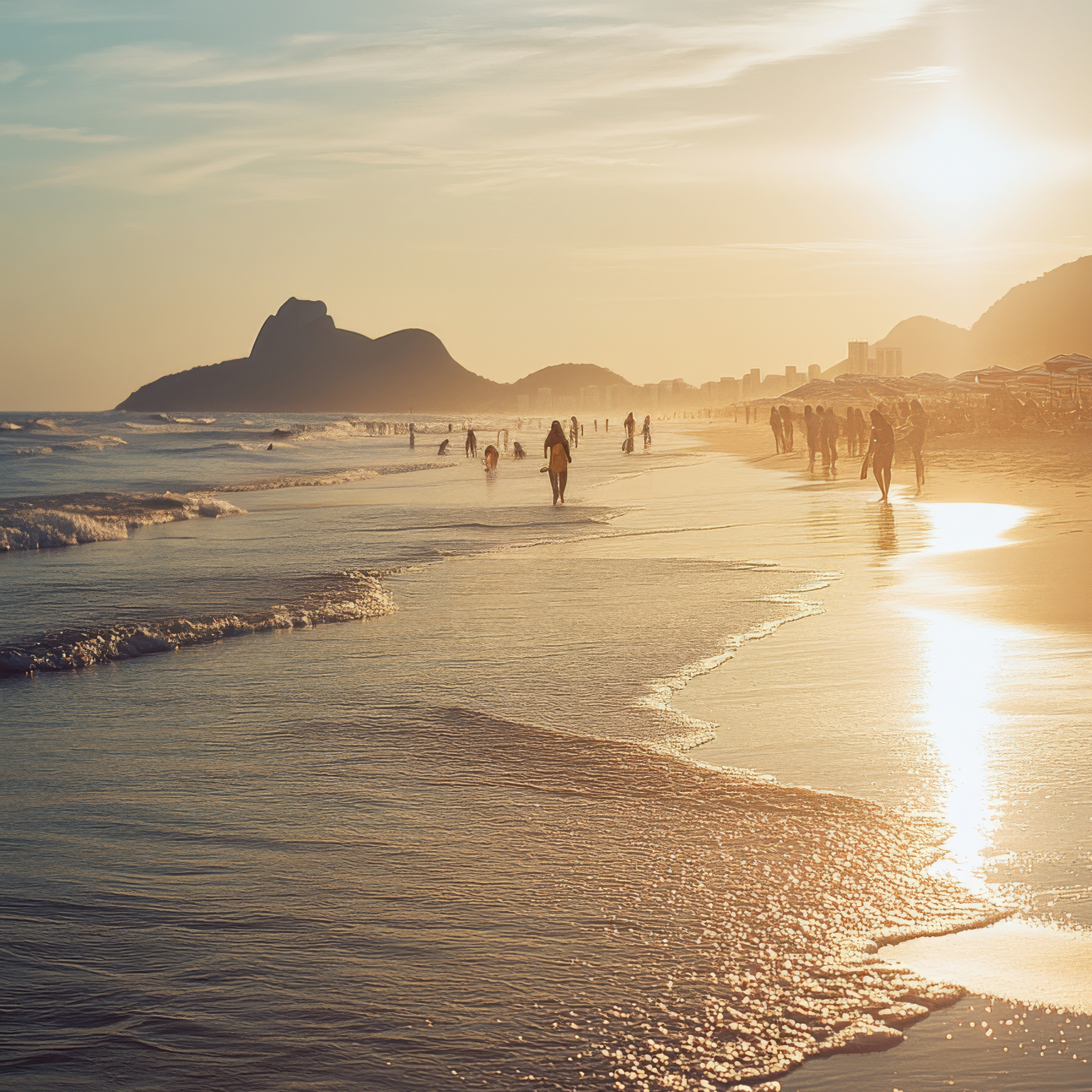 Ocean beach scene at sunset with multiple people wading in the water, waves washing onto the shore, and mountains on the horizon.