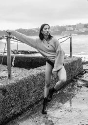 Woman in knit sweater and boots leaning on a coastal barrier wall by the ocean