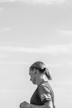 Black and white profile portrait of a woman with a ponytail against an overcast sky by Luke