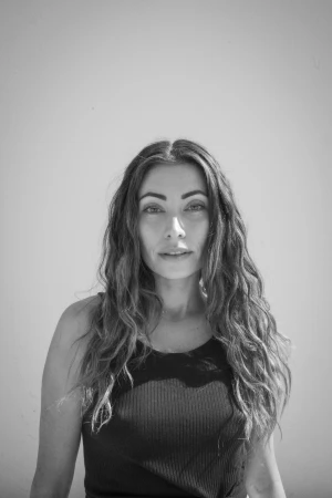 Portrait of a woman with long wavy hair wearing a dark tank top against a plain light background captured by photographer Luke.