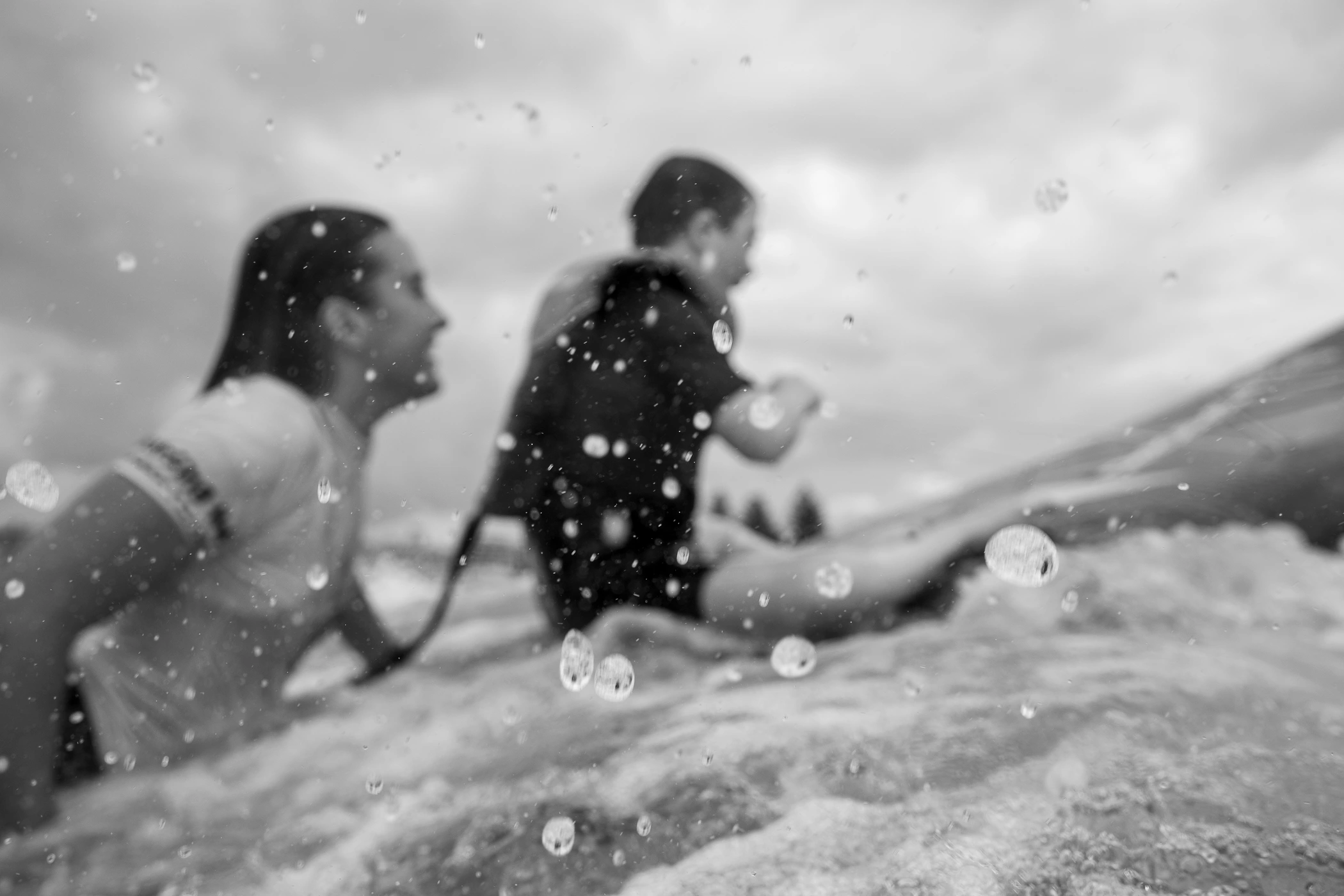 Black and white action photograph of two people in water with splashing water droplets in the foreground.