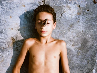 Young boy lying on a rough stone surface with a butterfly resting on his face