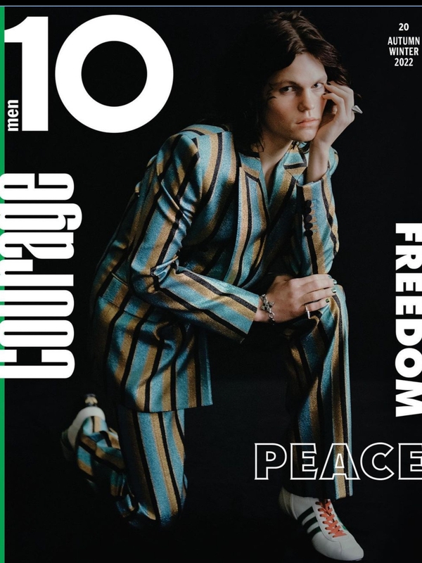 Magazine cover featuring a male model in a striped suit, kneeling against a dark backdrop, with magazine text elements in the frame.