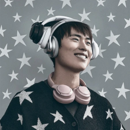 Young man smiles wearing white and pink headphones, adorned in a star-patterned cardigan against a backdrop of star shapes.