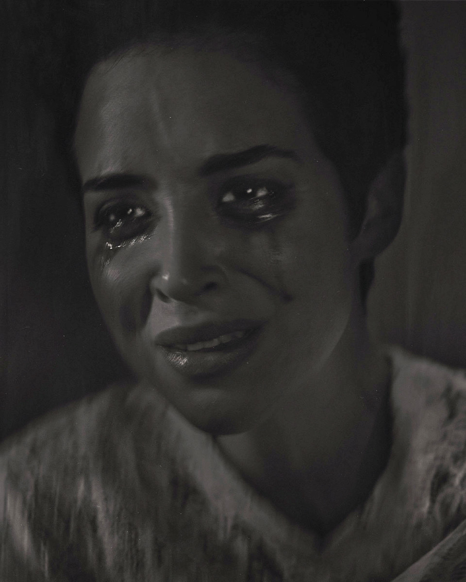 Close-up portrait of a young adult woman with tears streaming down her face. She has short dark hair and is wearing a light-colored shirt.